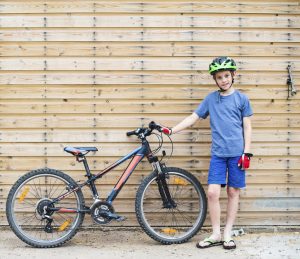 A boy with his bike that use both front and back shocks. This set of shock absorbers improves the comfort of a bicycle or rough trail ride.