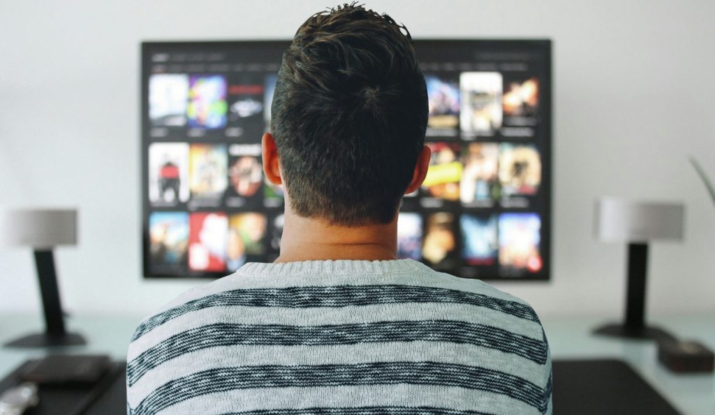 A person sitting on a comfortable sofa, engrossed in watching tv- a flat screen tv.