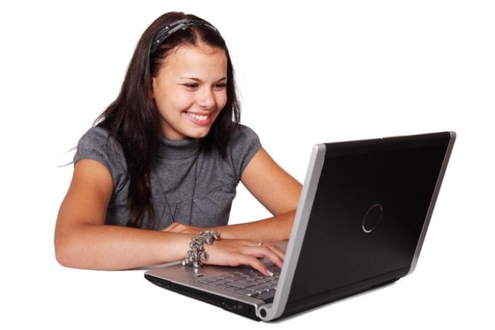 A girl with a black hair wearing a hair band and a gray blouse is browsing the net using a PC with matching colors of black and gray.