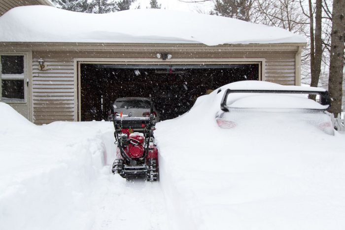 A house full of snow with a snow blower machine doing its best in clearing the entrance