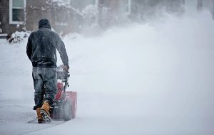 a man is doing his best in clearing the road full of snow using a snow blower on a snowy morning