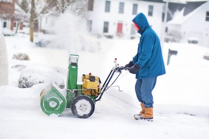 A man wearing a blue coat on a snowy season driving a best snow blower