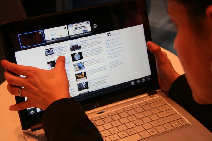 A woman is using a touchscreen laptop. She is using her fingers to navigate the webpage. This best touchscreen laptop has metallic design keyboard. The woman is wearing a ring. The woman is navigating the website easily because of the best touchscreen capability of the laptop. 