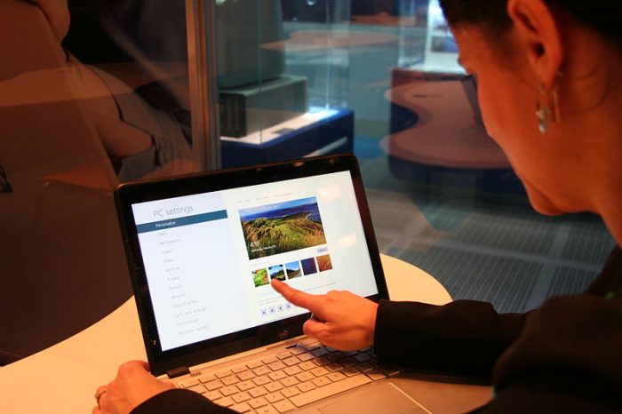 A woman is using her best touchscreen laptop. She is using his fingers to navigate it.