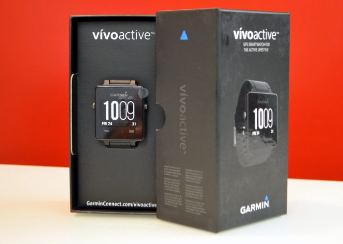 Garmin: Garmin Vivoactive watch presented next to its box on a table with a red backdrop.