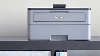 A gray printer is on the top of the shelf. The brand is Brother, one of the best cheap printers out there. 