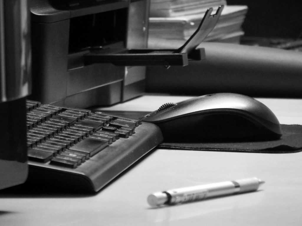 A table with mouse, pen, keyboard, and printer. All the materials on the table are black and best for office work. 