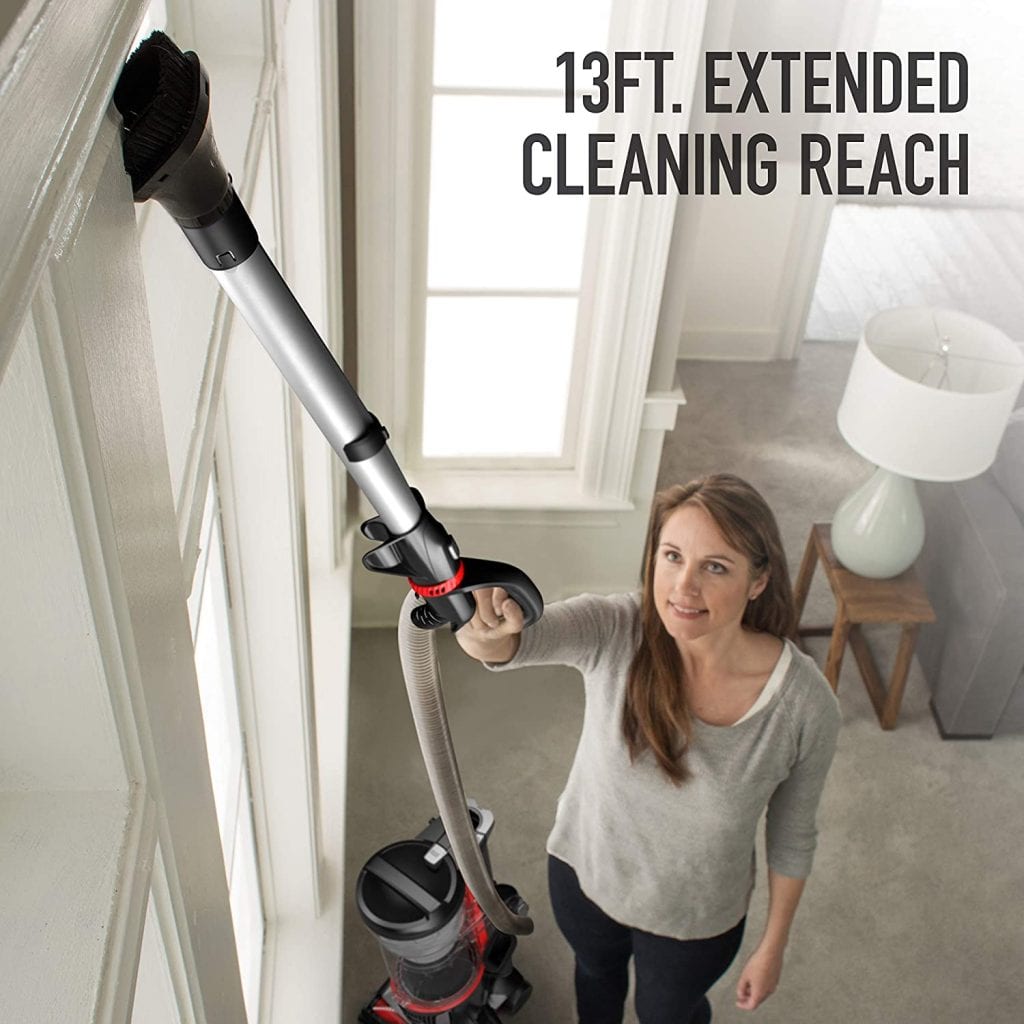 A woman using a vacuum cleaner to clean the walls of her room. She is using an extendable attachment to reach high places.