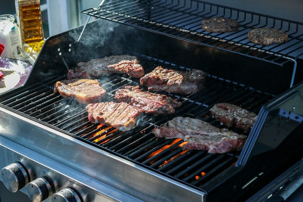 The image showcases a BBQ in full swing, capturing the special essence of outdoor cooking. Seven succulent steaks with perfect grill marks sizzle atop the grill, exuding an irresistible aroma. Flare-ups lick the edges of the meat, hinting at the high heat of the grill. The best part of grilling is the art of the char, clearly mastered here as evidenced by the delectable crust on each steak. To one side, four burger patties await their turn to grill to perfection. This BBQ scene epitomizes the best gatherings where the grill becomes a focal point, and grill transforms simple ingredients into culinary delights.