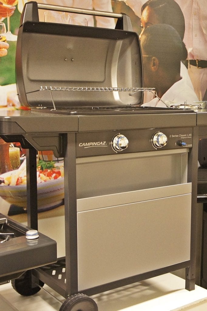 The image features a modern, stainless steel grill, unlit and clean, poised for the best grill experience. Its spacious grill hood is open, revealing the grill's ample cooking area, ready to accommodate a feast. Below the grill, a cabinet offers storage, perhaps for grilling tools or spices. The grill is mounted on a sturdy cart with wheels, designed for easy mobility. Two prominent dials on the front hint at precise heat control for grilling perfection. On the side, a small shelf could serve as a prep area. This grill represents the potential of memorable grilling moments, a beacon for grill enthusiasts.
