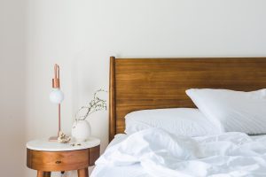 Perfect Down Comforter: A neatly-made bed featuring a down comforter, complemented by a wooden headboard and a stylish bedside lamp, creating a tranquil bedroom setting. The room's aesthetic is completed by the minimalist decor, which brings a sense of peace and sophistication.