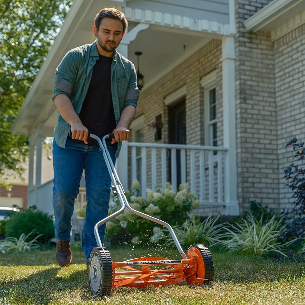 An American Lawn Mower Company reel mower is being used by a man in the front yard. Orange reel mower.