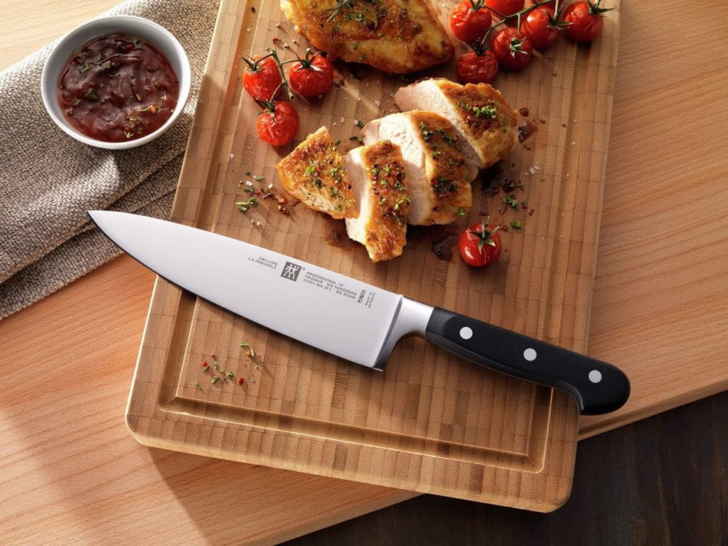 There is a sharp point chef's best knife on the chopping board. You can also see that there are slices of bread, dried tomatoes and a dip. 