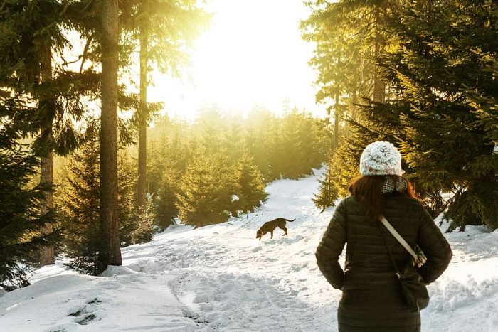 A woman is wearing a down coat while walking on the woods.