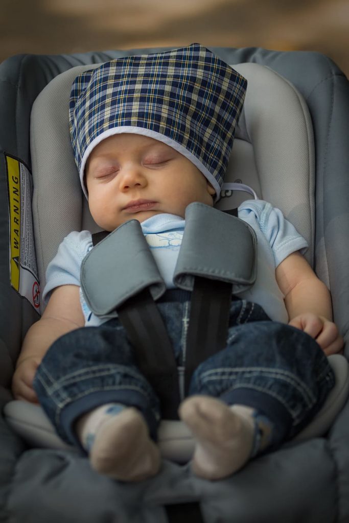 Infant car seat: A serene infant asleep in a car seat, snugly secured by padded straps, wearing a blue onesie and a checkered hat, evoking a sense of peace and safety. Perfect infant car seat.