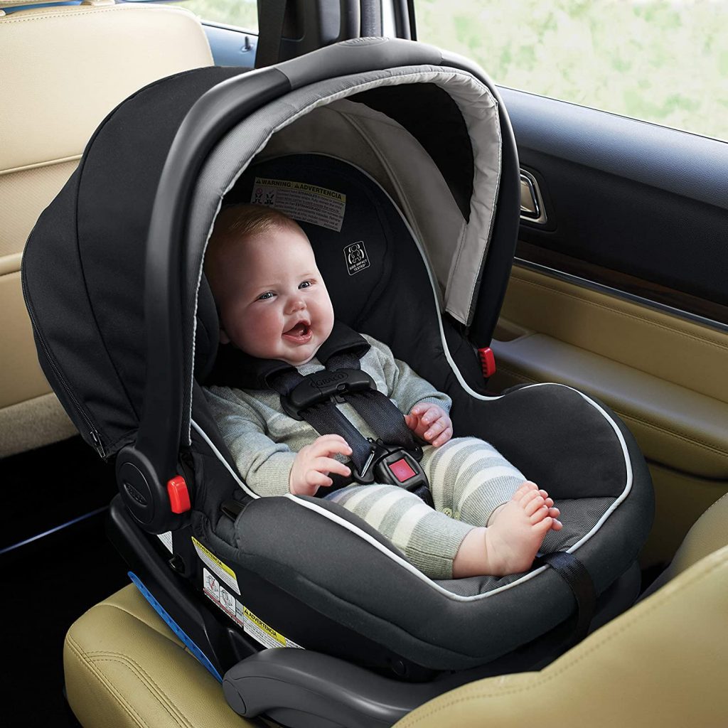 Best car seat for an infant: A joyful infant with a wide smile, secured in a black and gray rear-facing car seat with an adjustable canopy, inside a vehicle with a tan leather interior. Perfect infant car seat.