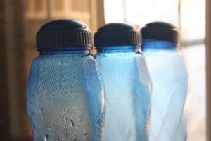 Water bottles in blue and black for trips are placed near the window of the room. These essentials are for keeping hydrated while traveling.