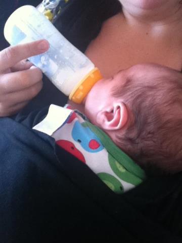 A mother feeding her baby with formula in a bottle.