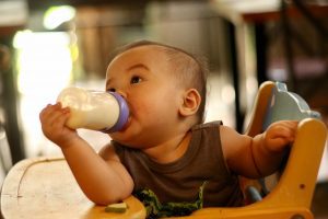 A little child sits independently on his chair while drinking his Loulouka formula, one of the best formula brands.