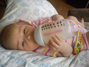 An infant holding a bottle of formula milk. 