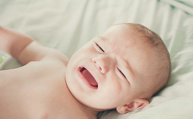 A crying baby lying on the bed