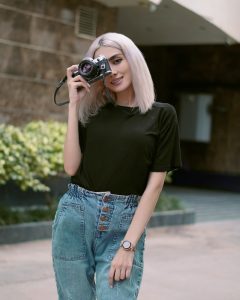 A woman wearing her summer outfits, while holding a camera and is smiling.