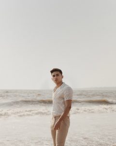 Outfits for the season. A man wearing a white polo while standing in a beach. Look for great outfits that are comfortable, outfits tailored perfectly for the hot season.