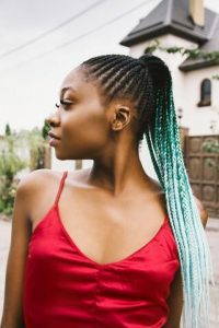 A beautiful girl in a red dress, flaunting her long braided tresses as one of the best hairstyles, showcasing a light emerald and teal-white gradient color blend that perfectly complements her attire.