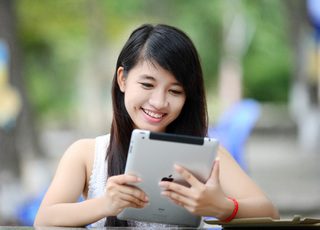 A young woman enjoying her summer vacation by reading jokes on her tablet in the park.