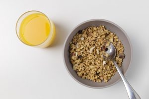 A glass of orange juice full of vitamin C and a bowl of cereal full of vitamin b12.