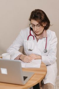 A doctor is sitting at a table and writing a prescription for prenatal vitamins.