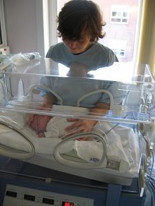 A mother holding her preterm baby. The preterm baby is inside an incubator.