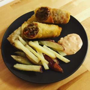 A black plate of air-fried cheeseburger egg rolls on top of kitchen table