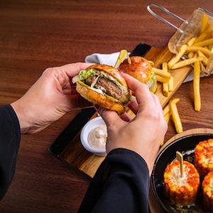 Hands holding an open air fried White Castle slider, revealing a beef patty, lettuce, and sauce, with fries, more air fryer sliders, and sauce dishes. Achieve this with an air fryer. Check other air fryer recipes.