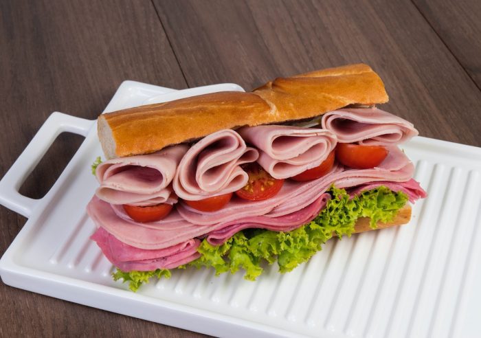 A tasty sandwich on a serving tray. The sandwich has meat, tomatoes, and lettuce.