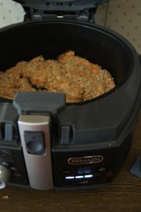 An air fryer basket filled with breaded chicken fillets, ready to be cooked, with the air fryer handle and control panel in view.