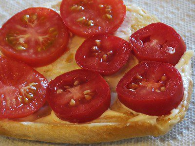 Sliced ripe tomato could be improved with the addition of fresh lettuce leaves, arranged on a slice of whole-grain bread, making it ready to be assembled into a sandwich.