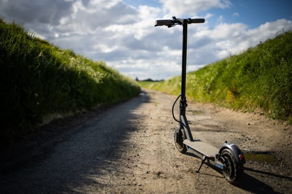 A black scooter without an owner is parked in the middle of the road with a lot of grass on its side.