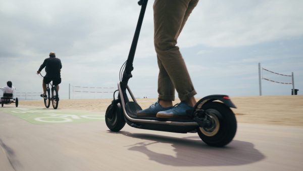 A man is riding a scooter with its new applied deck tape. His scooter has large wheels perfect for a safe and fun ride on a sunny morning.