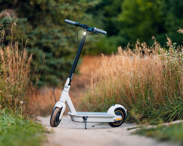 A color combined black and white scooter is parked on a bumpy surface with grasses all around it.
