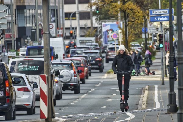 The man wearing jacket is casually riding his scooter on the road