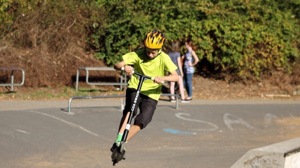 The boy in a yellow shirt is manifesting his scooter tricks 