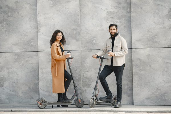 A man and a woman are riding their scooters while having smiles on their faces.
