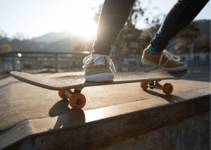 A picture of two feet riding a skateboard. The person is wearing orange shoes with white lace. This picture was taken in skateboard park. 
