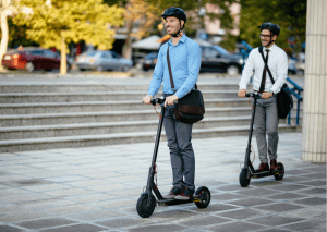 Best two helmeted men wearing sling bags smile while each enjoying the ride on their best scooter outdoors.