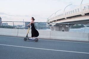 A woman in black rides her scooter, traveling down the road in style.