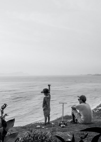 A man and a child looking out at a body of water with a scooter parked next to them