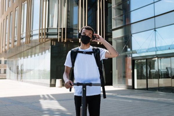 A man wearing a mask and headphones while holding his scooter's handlebars