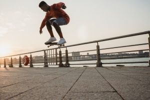 A young skateboarder confidently glides across a smooth concrete skatepark, their body poised and balanced on the skateboard. The sun casts a warm glow on the vibrant graffiti-covered skateboard ramps and rails in the skate background. With each skillful skateboard maneuver, the skateboarder exudes a sense of self-assurance, embodying the essence of building confidence by the exhilarating sport of skateboarding.