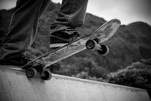 A determined skateboarder on his skateboard as he attempts his inaugural trick. The sun casts a warm glow on the skatepark. With one foot firmly planted on the skateboard and the other ready to skateboard flick, he prepares to execute his first ollie, the skateboard wheels poised for mid-air action. The background showcases a mix of concrete ramps and rails, echoing the energy of the skater's daring endeavor.